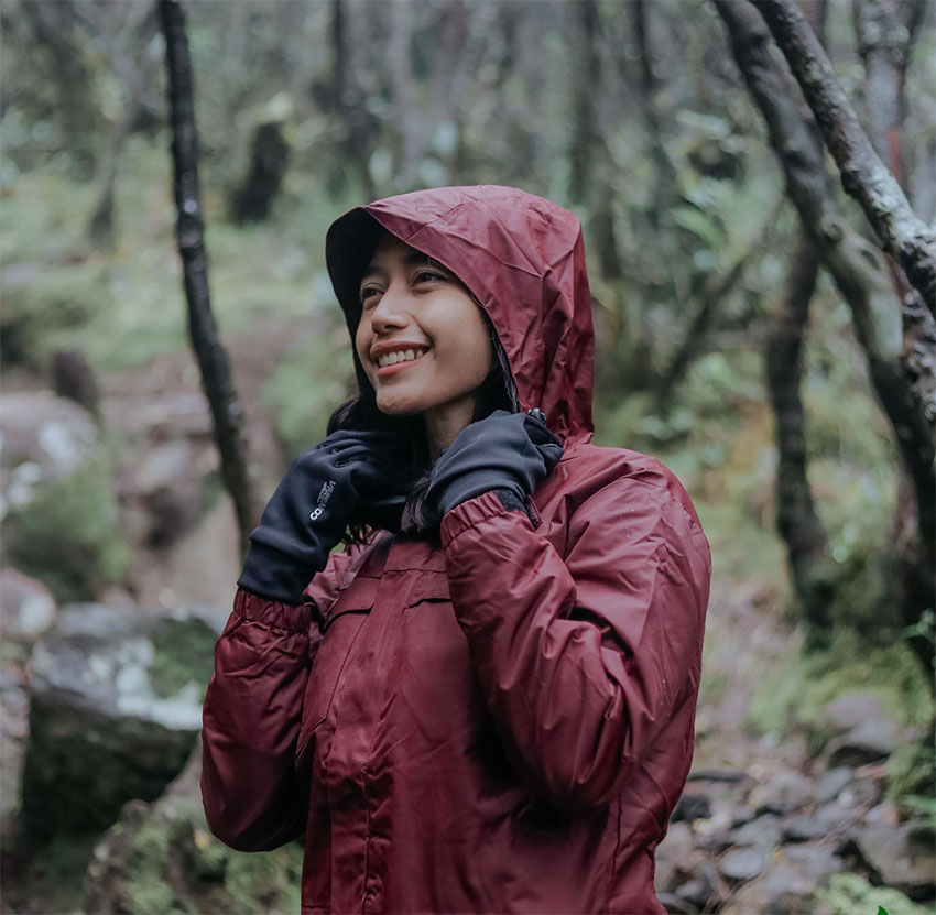 Outfit Gunung Wanita Hijab mengenakan Jaket Gunung Tahan Air dan Angin produk Consina warna maroon dengan sarung tangan hitam saat mendaki di hutan lembab — sumber foto consina.com