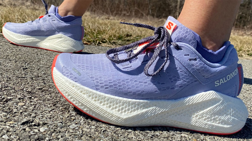 Close-up Running Shoes Wanita Terbaik 2025 Salomon Aero Glide 3 warna ungu dengan midsole putih dan outsole merah saat digunakan berjalan di jalan aspal — sumber foto weartesters.com