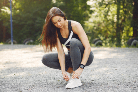 Wanita mengikat tali sepatu running putih di area outdoor. (Sumber foto: Freepik)