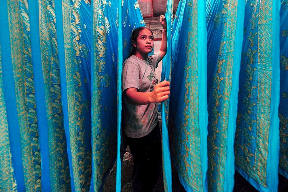 Perajin merapikan beberapa lembar kain batik bermotif aksara incung Kerinci yang dijemur di tempat produksi batik Daun Sirih Desa Simpang Tiga, Sungai Penuh, Jambi, Senin (16/9/2024): bisnis.com