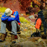 Pendaki gunung beristirahat di jalur berbatu karena kelelahan dan gejala Acute Mountain Sickness (AMS)